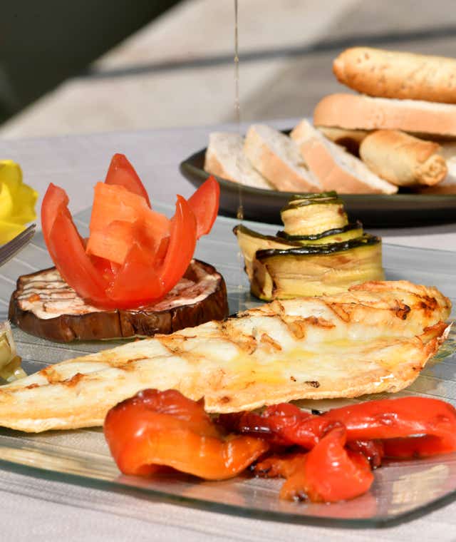Filetto di pesce servito su un piatto semitrasparente con melanzane e zucchine, in uno dei nostri tavoli esterni